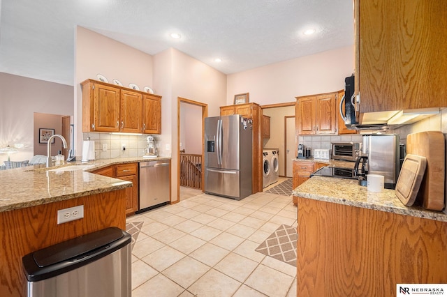 kitchen featuring light stone counters, light tile patterned flooring, a sink, appliances with stainless steel finishes, and washer and clothes dryer