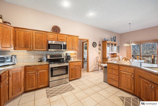 kitchen featuring a toaster, decorative backsplash, brown cabinets, hanging light fixtures, and stainless steel appliances