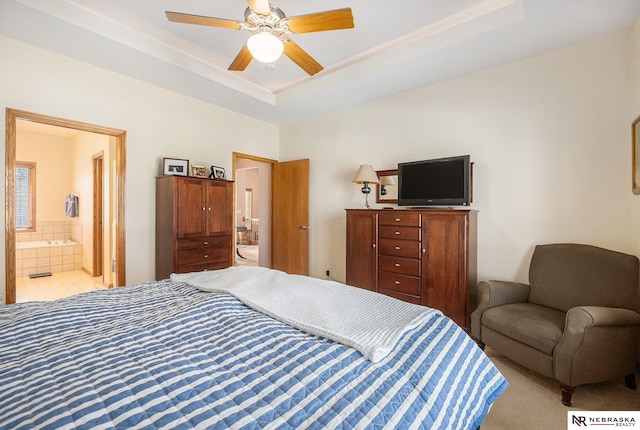 bedroom featuring a raised ceiling, ensuite bathroom, and ceiling fan