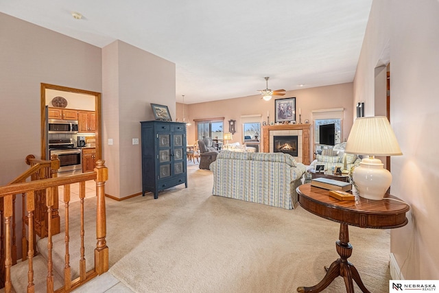 living room featuring a fireplace, a ceiling fan, baseboards, and light carpet