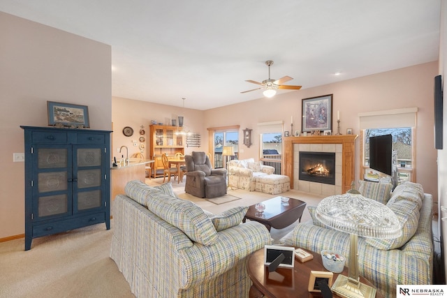 living area featuring baseboards, light carpet, ceiling fan, and a tiled fireplace