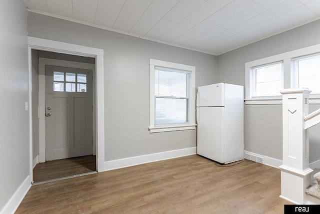 foyer entrance with visible vents, baseboards, light wood-style floors, and crown molding