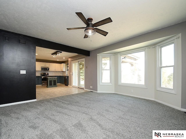 unfurnished living room with plenty of natural light, a ceiling fan, light colored carpet, and a textured ceiling