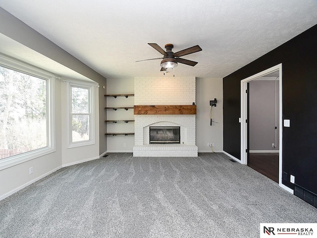 unfurnished living room with a textured ceiling, carpet, baseboards, a brick fireplace, and ceiling fan