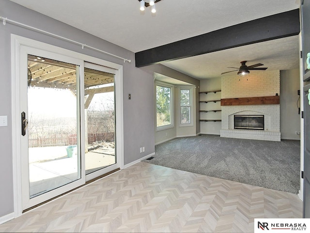 unfurnished living room featuring baseboards, beam ceiling, ceiling fan, a textured ceiling, and a brick fireplace