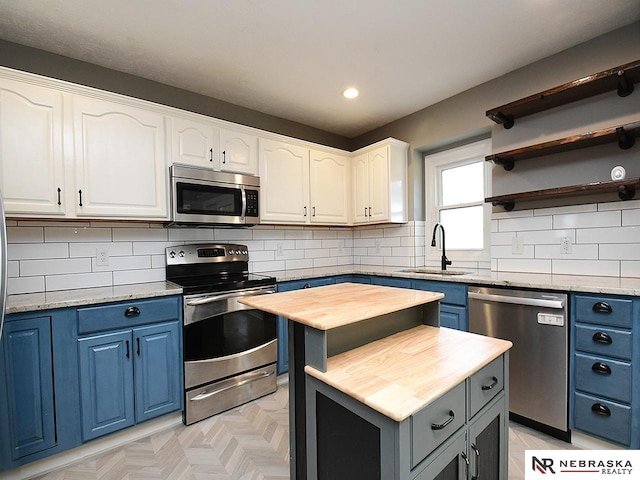 kitchen with blue cabinets, a sink, white cabinetry, stainless steel appliances, and butcher block counters