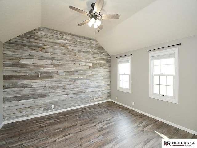 empty room with wooden walls, an accent wall, vaulted ceiling, wood finished floors, and a ceiling fan