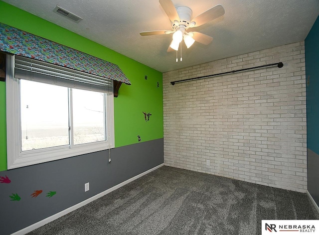 unfurnished room featuring visible vents, brick wall, carpet flooring, a textured ceiling, and a ceiling fan