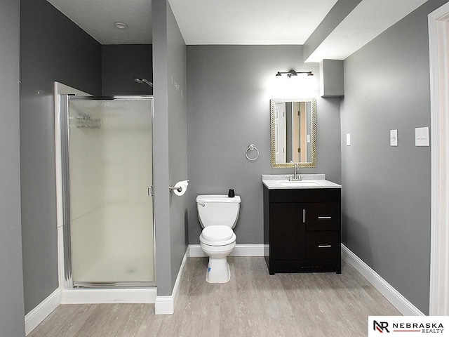 bathroom with a shower stall, baseboards, toilet, wood finished floors, and vanity