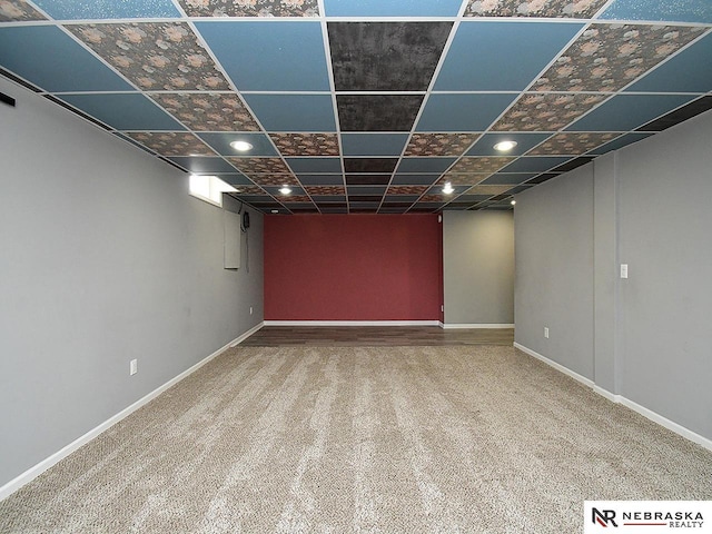 finished below grade area featuring baseboards, a paneled ceiling, and carpet