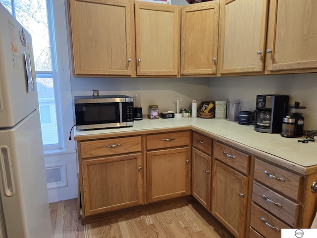 kitchen featuring stainless steel microwave, light countertops, freestanding refrigerator, and light wood-type flooring