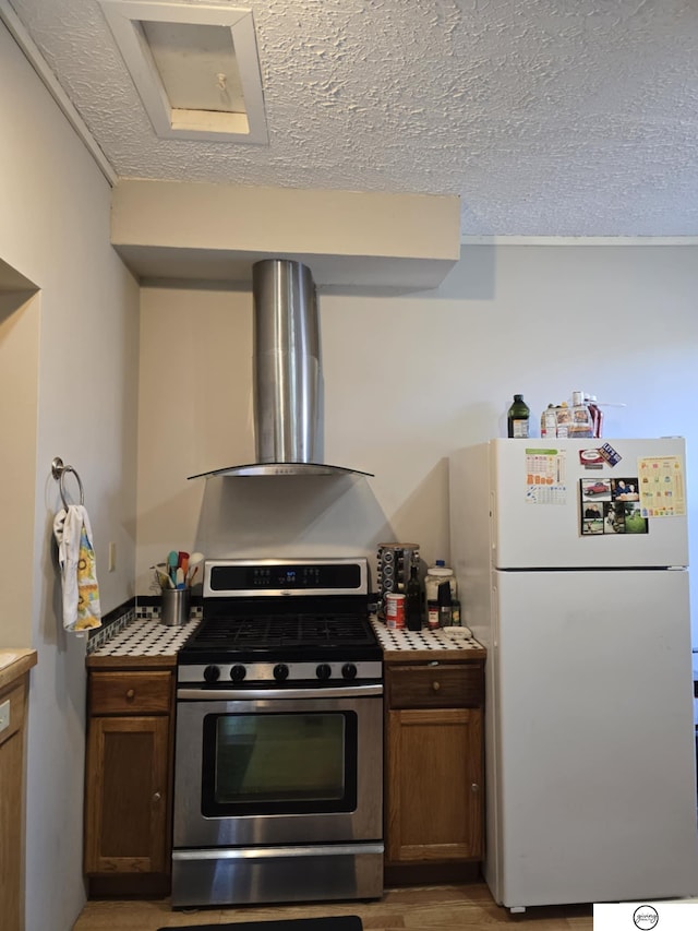 kitchen featuring freestanding refrigerator, light wood-style floors, a textured ceiling, gas range, and wall chimney exhaust hood