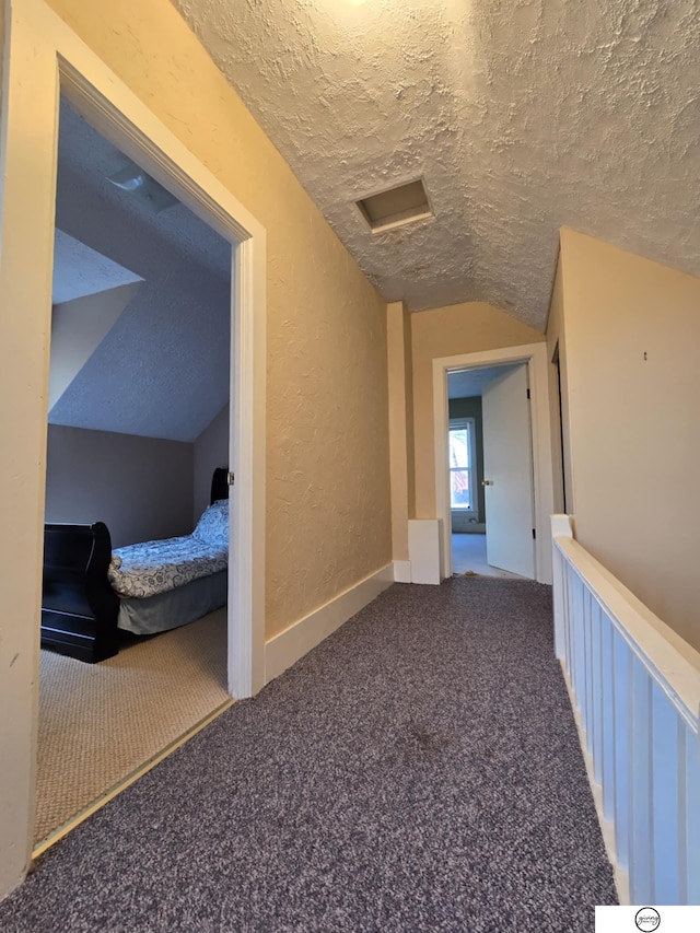 corridor with carpet floors, a textured ceiling, vaulted ceiling, and a textured wall