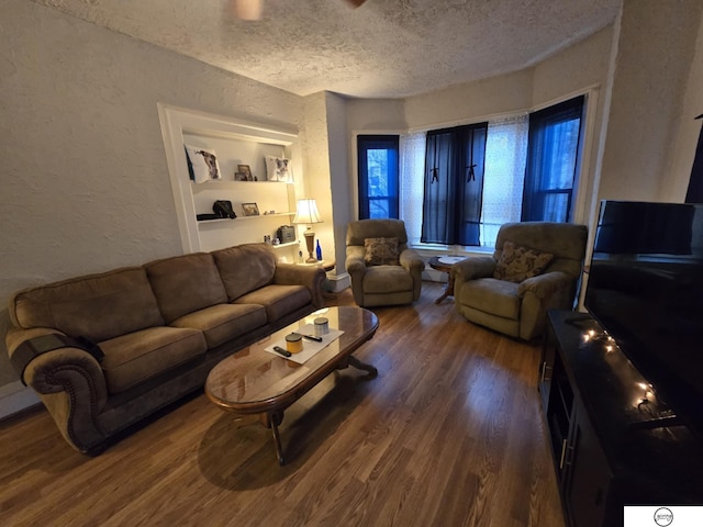 living area with dark wood-type flooring, built in shelves, a textured wall, and a textured ceiling