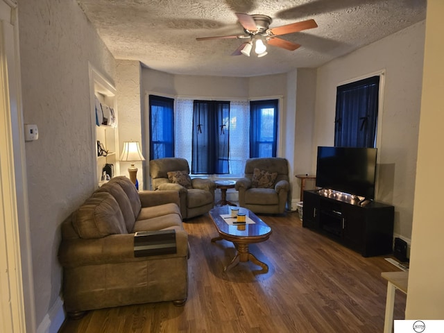 living area featuring baseboards, ceiling fan, wood finished floors, a textured wall, and a textured ceiling