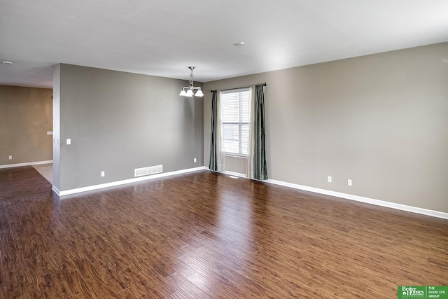 empty room featuring dark wood finished floors, a notable chandelier, baseboards, and visible vents