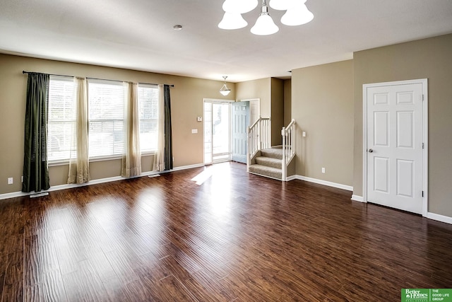 unfurnished living room with stairway, a notable chandelier, baseboards, and dark wood-style flooring