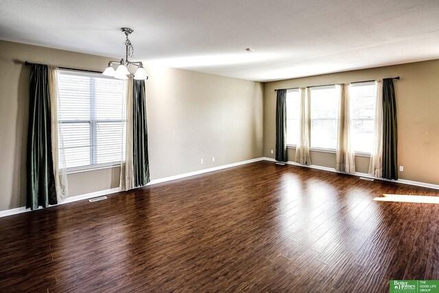 empty room featuring a chandelier, visible vents, baseboards, and dark wood-style flooring