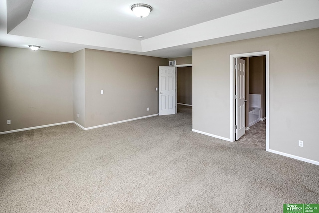 carpeted empty room with a tray ceiling, visible vents, and baseboards