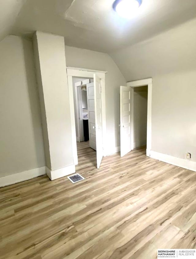 additional living space with visible vents, light wood-type flooring, baseboards, and vaulted ceiling