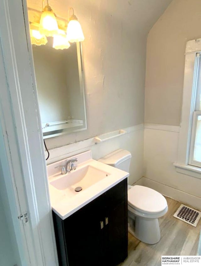 half bathroom with visible vents, toilet, vanity, and wood finished floors