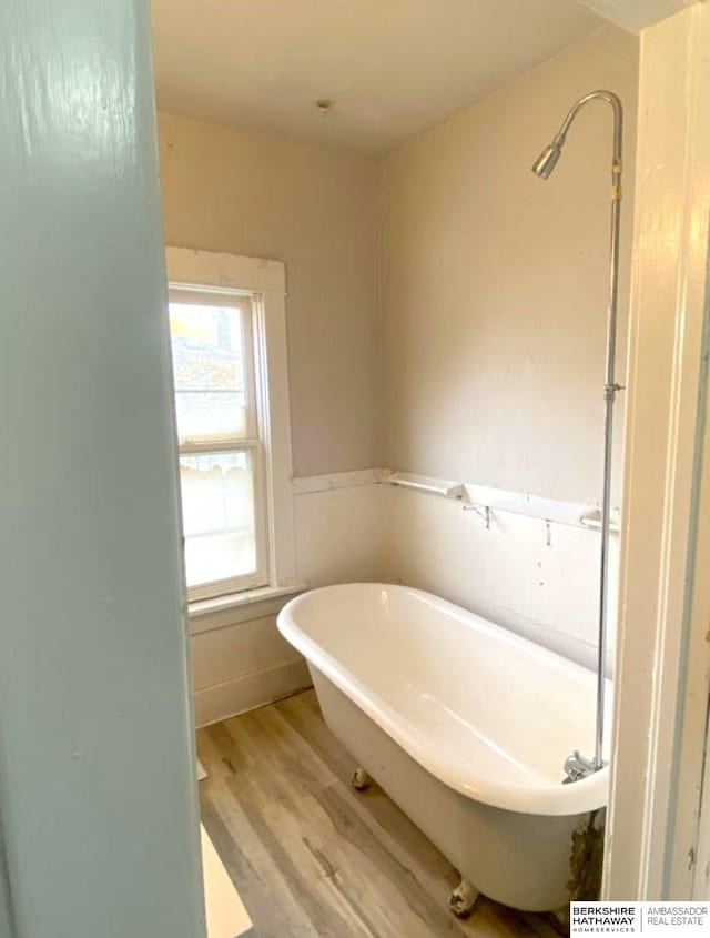 bathroom with a soaking tub, wood finished floors, and wainscoting