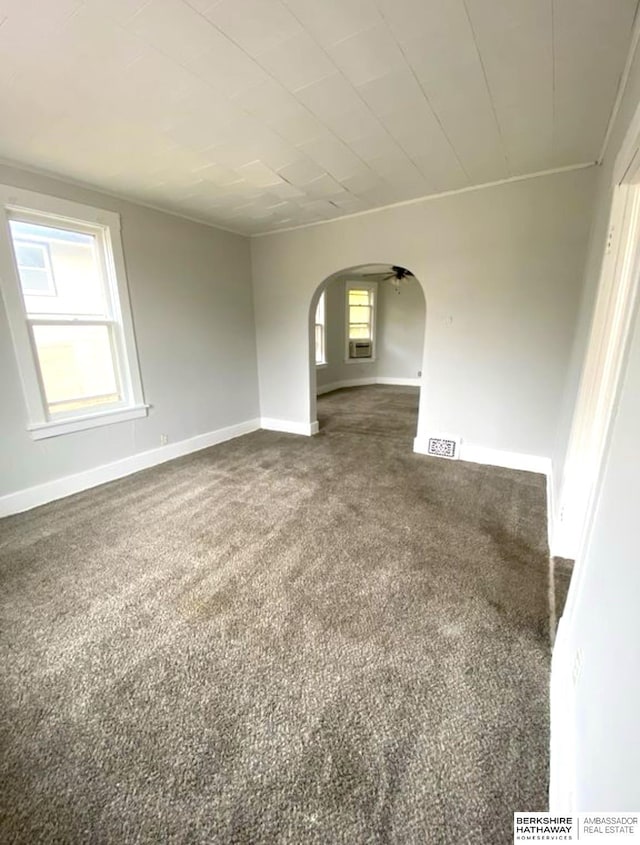 spare room with arched walkways, visible vents, baseboards, and dark colored carpet