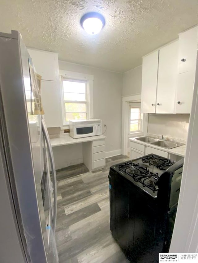 kitchen featuring black gas range oven, white microwave, light wood-style flooring, freestanding refrigerator, and white cabinetry