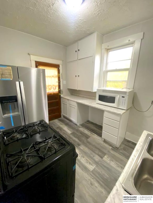 kitchen with wood finished floors, white microwave, stainless steel fridge with ice dispenser, black gas range, and a textured ceiling