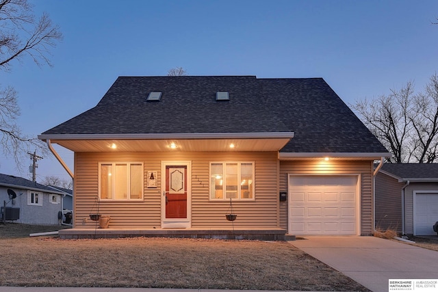 view of front of house featuring central AC unit, an attached garage, a shingled roof, and driveway