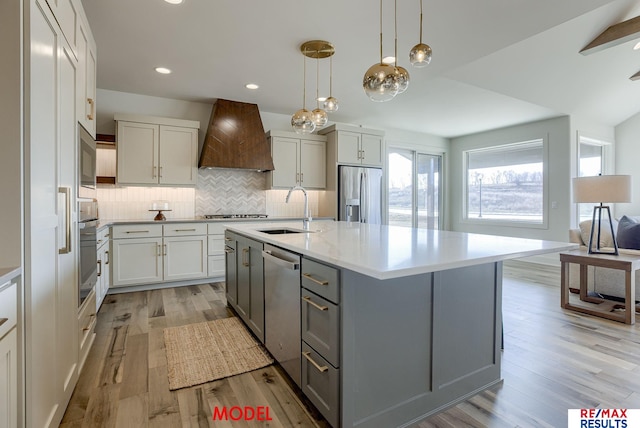 kitchen with premium range hood, gray cabinets, a sink, stainless steel appliances, and light wood-style floors