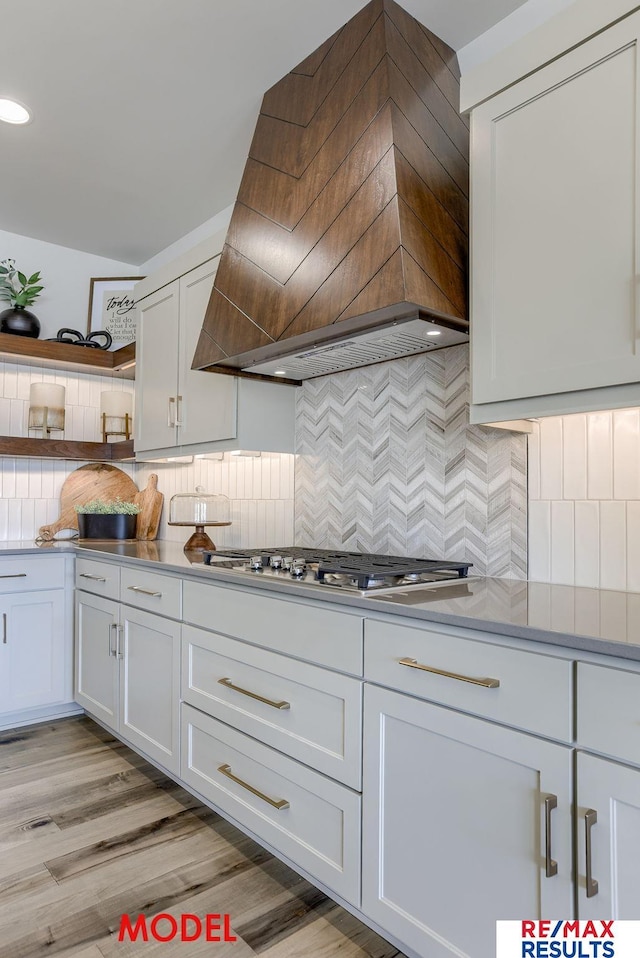 kitchen featuring light wood-type flooring, custom range hood, open shelves, tasteful backsplash, and stainless steel gas cooktop