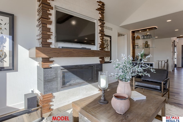 living room with vaulted ceiling, a glass covered fireplace, visible vents, and wood finished floors