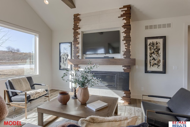 living room featuring visible vents, wood finished floors, lofted ceiling, and a glass covered fireplace