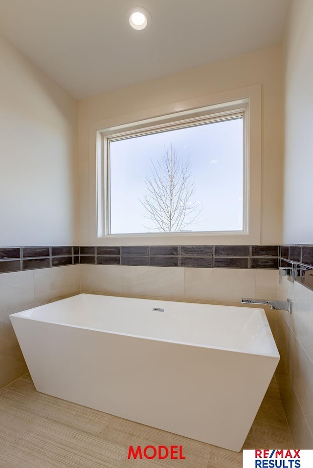 bathroom with recessed lighting, a freestanding tub, tile walls, and a healthy amount of sunlight