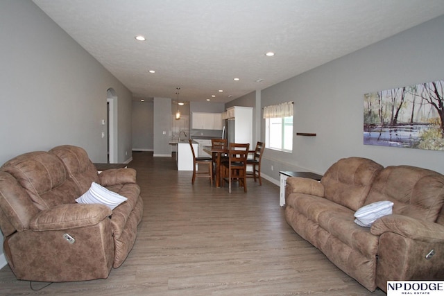 living area with arched walkways, recessed lighting, baseboards, and light wood-style floors