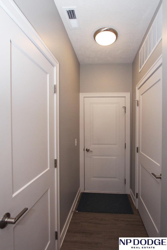 corridor with visible vents, baseboards, a textured ceiling, and dark wood-style flooring