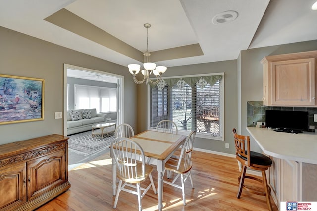 dining area with baseboards, a raised ceiling, an inviting chandelier, and light wood-style flooring