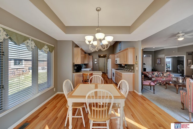 dining space featuring light wood-type flooring, a tray ceiling, and baseboards