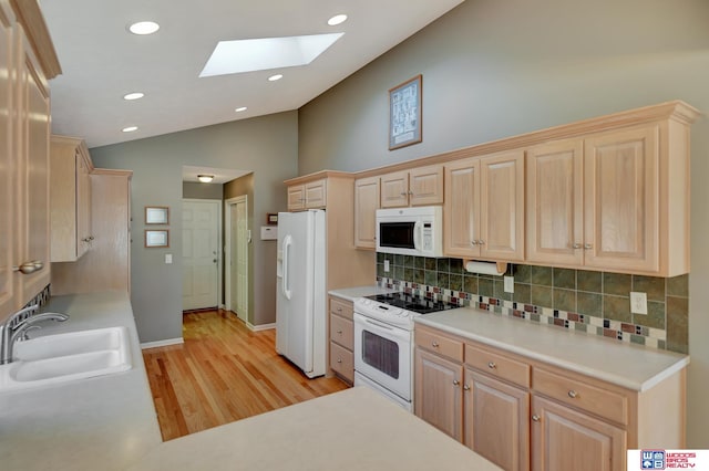 kitchen with light brown cabinets, light countertops, vaulted ceiling with skylight, white appliances, and a sink