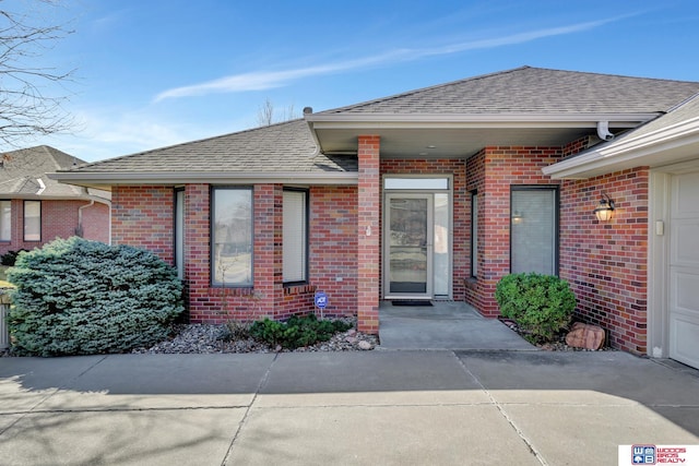 view of exterior entry with brick siding and a shingled roof