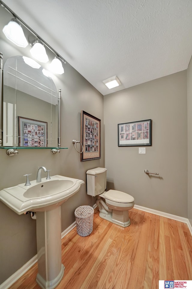 bathroom with toilet, wood finished floors, baseboards, and a textured ceiling