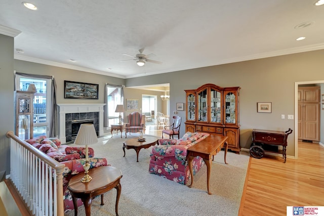 living room featuring light wood-type flooring, crown molding, baseboards, ceiling fan, and a tile fireplace