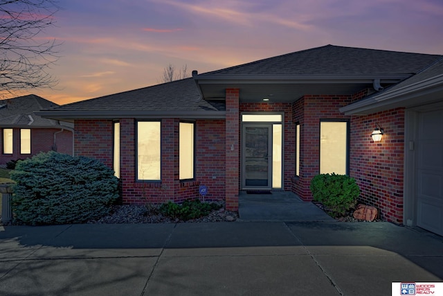 view of front facade featuring brick siding, concrete driveway, and roof with shingles