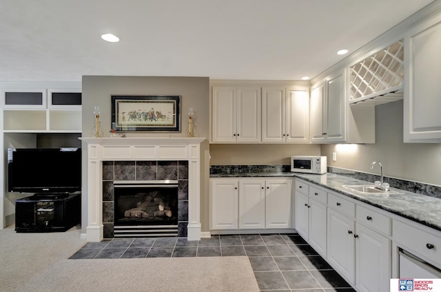 kitchen with a sink, recessed lighting, white cabinets, white microwave, and a tile fireplace