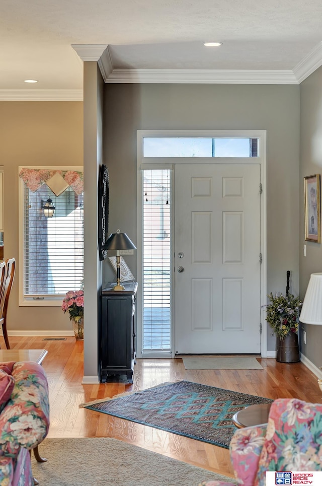 foyer featuring visible vents, wood finished floors, baseboards, and ornamental molding