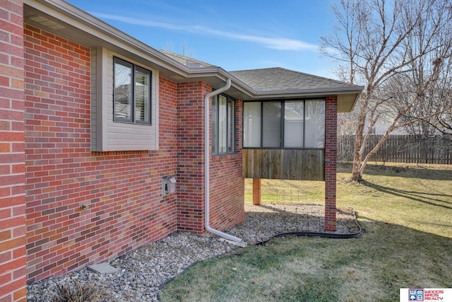 exterior space featuring a yard, fence, brick siding, and roof with shingles