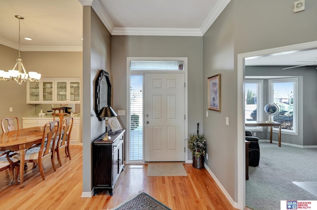 foyer with light wood finished floors, baseboards, crown molding, and an inviting chandelier