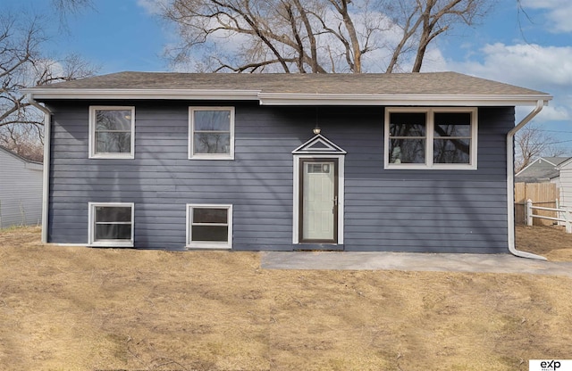 split foyer home featuring fence and a shingled roof