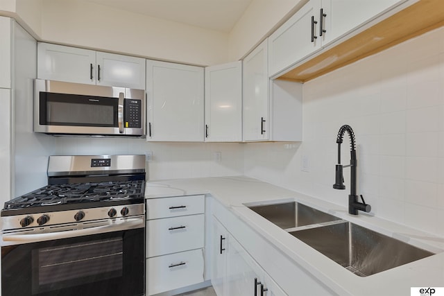 kitchen featuring tasteful backsplash, white cabinets, appliances with stainless steel finishes, and a sink